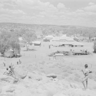 A black and white photograph of The Bungalow taken from a nearby hill. There are a group of young children playing.