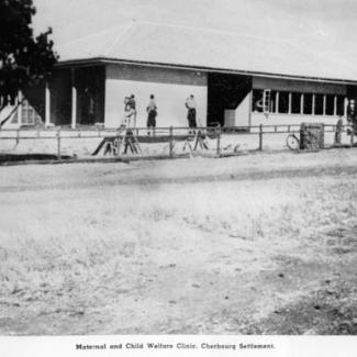 A black and white photograph of a building at Cherbourg Dormitory. There is a small group of people standing in front of the building.