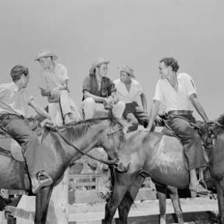 A black and white photograph of a group of young men at Croker Island Mission. Three are sitting on a fence, while two are on horseback.